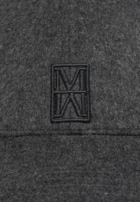 Graue Filzkappe mit einem schwarzen bestickten Logo in Form eines "M" innerhalb eines rechteckigen Rahmens. Strukturiert Oberfläche, schlichtes Design.