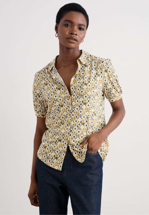 Short-sleeve button-down shirt in yellow with blue geometric floral patterns, cotton material, and a relaxed fit. Details include a pointed collar.