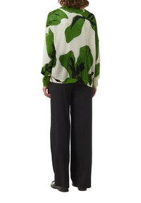 Groene en witte oversized trui met een bladdessin, met lange mouwen en een ronde halslijn, gecombineerd met zwarte wijde broek.