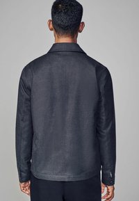 Ciemnoszara kurtka z gładkiego, fakturowanego materiału. Posiada kołnierz z rozłożonymi klapami, długie rękawy i mankiety zapinane na guziki. Prosty, minimalistyczny design.