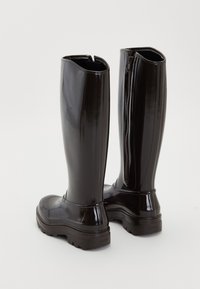 Par de botas altas y brillantes de color negro con suelas gruesas y cremallera trasera visible, situadas sobre un fondo blanco sencillo.