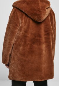 Brun faux fur frakke med hætte, der har en blød tekstur og en løs pasform, der strækker sig til midt på låret.