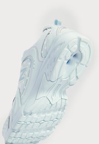 Vaaleansiniset urheilukengät, joissa on teksturoitu päällinen, jossa on pilkkuja ja virtaviivainen muotoilu. Pohja on kuvioitu pidon parantamiseksi.