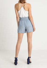 Shorts bleu clair avec une taille élastique, assortis à un débardeur blanc à fines bretelles, présentant une coupe décontractée et une texture douce.