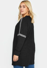 Svart lång kofta med ribbad textur. Utsmyckad med rhinestones på ärmarna och har en avslappnad passform. Designad med rund halsringning och långa ärmar.