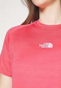 Růžové sportovní tričko vyrobené z lehkého materiálu, s krátkými rukávy a kulatým výstřihem. Na hrudi je vyšívané logo značky The North Face.