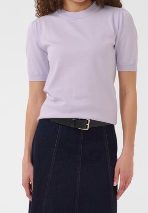 Vrouw draagt een lichtpaarse top met korte mouwen en pofschouders, ingestopt in een donkere denim rok met een zwarte riem.