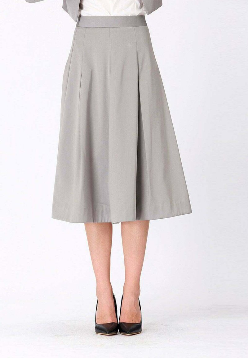 Jupe plissée grise avec une taille ajustée, longueur genoux, en tissu doux. Associée à des chaussures à talons hauts noires.