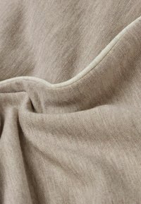 Lys beige stof med subtil tekstur og en glat overflade. Har en kontrasterende hvid kant langs sømmen. Materialet synes blødt og faldende.