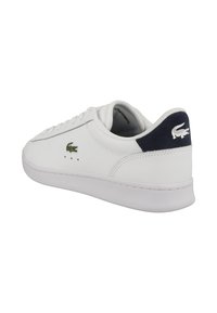 Baskets basses blanches avec logo crocodile vert sur le côté et logo crocodile blanc sur la languette de talon bleu marine, vues de dos.