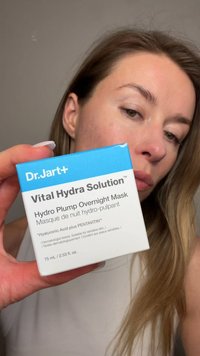 Femme tenant près de son visage la boîte du masque de nuit Dr.Jart+ Vital Hydra Solution Hydro Plump, sur un fond neutre.