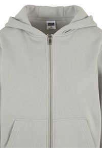 Sweat à capuche gris clair zippé avec poches avant, fermeture éclair visible et capuche attachée, étiqueté Urban Classics taille XS.