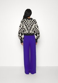 Pull en motif géométrique noir et blanc avec des manches bouffantes, associé à un pantalon large taille haute violet. Finition en tissu lisse.