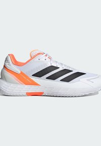 Λευκά αθλητικά παπούτσια με μαύρες ρίγες και πορτοκαλί λεπτομέρειες. Δικτυωτό επάνω μέρος με υφή, μαξιλαρωμένος γιακάς και καουτσούκ σόλα για πρόσφυση.