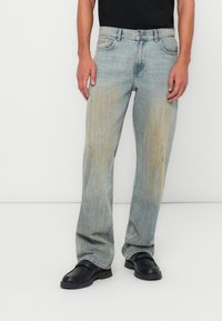Vervagende blauwe denim jeans met een recht gesneden pijp en lichte slijtage. Gecombineerd met zwarte instap schoenen. Eenvoudig zwart t-shirt erboven gedragen.
