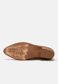 Tan suede shoe sole with a smooth finish, featuring a pointed toe and embossed text. The sole is brown with a light texture and a slight sheen.