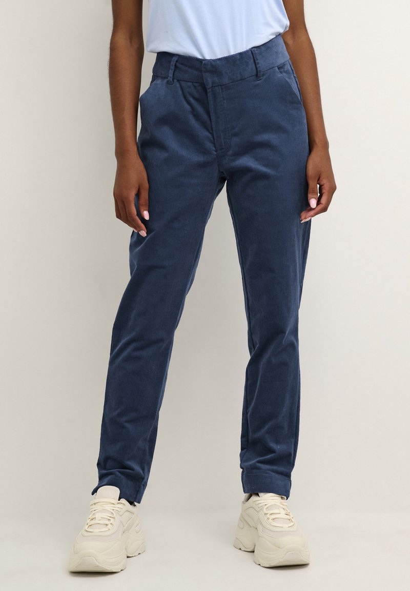 Navy corduroy broek met een recht gesneden ontwerp, voorzien van een middelhoge tailleband en zijzakken, gecombineerd met lichtgekleurde sneakers.