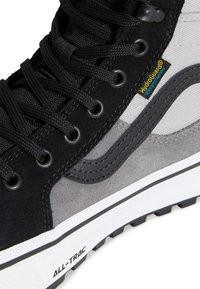 Primer plano de una bota de senderismo negra y gris con cordones negros, etiqueta HydroGuard a prueba de agua y suela blanca etiquetada como ALL-TRAC.