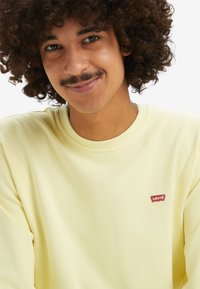 Lichtgele langemouwen T-shirt met een ronde hals en een klein rood Levi's-logo op de linkerbovenborst. Zachte stof met een gladde textuur.
