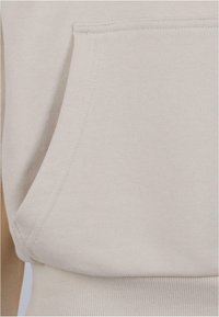 Lys beige sweatshirt med kengurulomme, ribbet ved håndleddene og kanten, lavet af en blød bomuldsblanding med en glat tekstur.