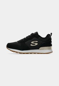 Sapatilha Skechers preta com sola branca, sola de borracha castanha, colarinho acolchoado, fecho com atacadores e logotipo "S" na lateral.