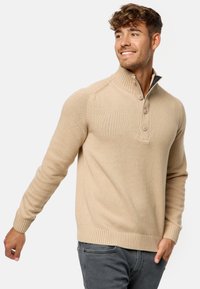 Pull-over en tricot beige avec un col montant, trois boutons, des poignets et un ourlet côtelés, présentant une texture lisse et une coupe ajustée.