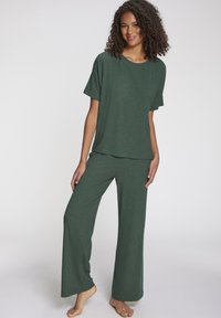 Zeleni rebrasti komplet za opuštanje koji se sastoji od majice s kratkim rukavima i širokih hlača. Mekana tekstura i ležeran kroj.