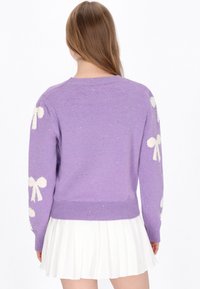 Lila Strickpullover mit weißen Schleifenmotiven, geripptem Saum und langen Ärmeln, mit subtilen Glitzerpartikeln im Stoff.