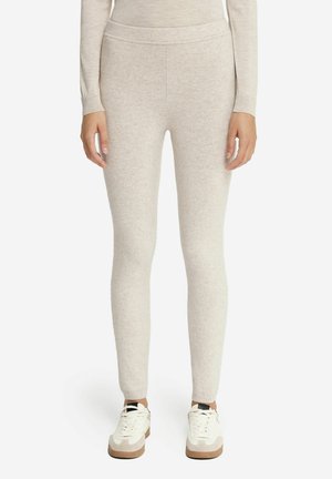 Lichtbeige nauwsluitende gebreide legging gedragen met een bijpassende top met lange mouwen en witte sneakers bij een persoon die rechtop staat.
