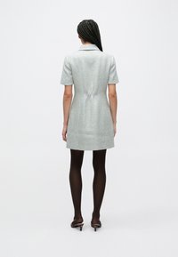 Kortärmad klänning till knäna i fiskbensmönstrat tyg, ljusblå och silverfärgade nyanser, med insvängd midja och slits bak, kombinerad med mörka strumpbyxor och klackar.