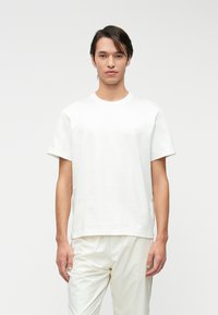 Λευκό μπλουζάκι κοντό μανίκι σε χαλαρή εφαρμογή, φτιαγμένο από βαμβάκι. Διαθέτει ριμπ λαιμό με στρογγυλή μορφή και μινιμαλιστική επωνυμία στο στήθος.