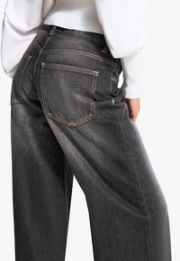 Dark grey wide-leg jeans with visible back pockets, contrasting orange stitching, and a textured denim fabric. Sit at the waist.