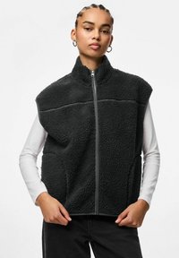 Melns vilnas vestes ar augstu apkakli, rāvējslēdzēja aizdari un sānu kabatām. Izceļas ar teksturētu audumu un kontrastējošām pelēkām šuvēm.