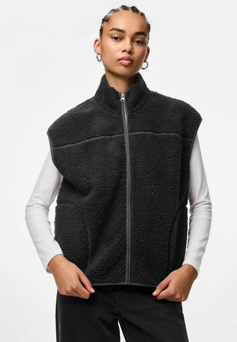 Melns vilnas vestes ar augstu apkakli, rāvējslēdzēja aizdari un sānu kabatām. Izceļas ar teksturētu audumu un kontrastējošām pelēkām šuvēm.