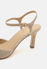 Sandale à talon haut en daim beige avec une bride à la cheville et une boucle dorée, dotée d’un bout arrondi et d’un talon effilé.