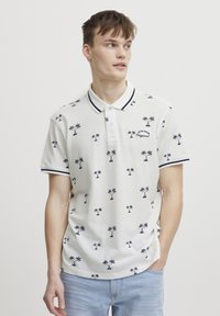 Hvit polo skjorte med marineblå palmetre mønster, ribbet krage og mansjetter, samt brodert "Original" detalj. Myk stoff, avslappet passform.