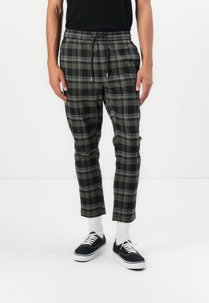 Kariert Jogginghosen in Schwarz, Grau und Olivgrün. Mit einem elastischen Bund und Kordelzug sowie schmal zulaufenden Beinen. Getragen mit schwarzen Turnschuhen.