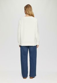 Witte oversized sweatshirt met verlaagde schouders, ribgebreide manchetten en zoom, gecombineerd met wijde blauwe denim broek. Eenvoudig ontwerp, geen zichtbare logo's.