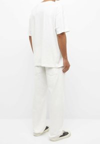 White cotton t-shirt with a loose fit, short sleeves, and a round neckline, paired with white relaxed-fit pants and black sneakers.