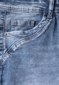Jeans en denim avec un lavage bleu clair, un dégradé subtil, un design à cinq poches et des coutures décoratives le long des coutures.