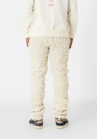 Crème-kleurige oversized broeken met een geweven textuurontwerp, voorzien van elastische boorden. Gecombineerd met zwarte en beige casual sneakers.