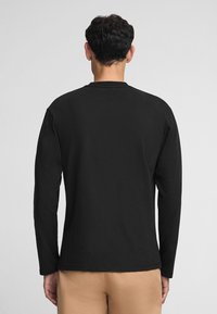 Czarna, długosługa koszulka z bawełny z okrągłym dekoltem i gładką fakturą, noszona z jasnymi spodniami.