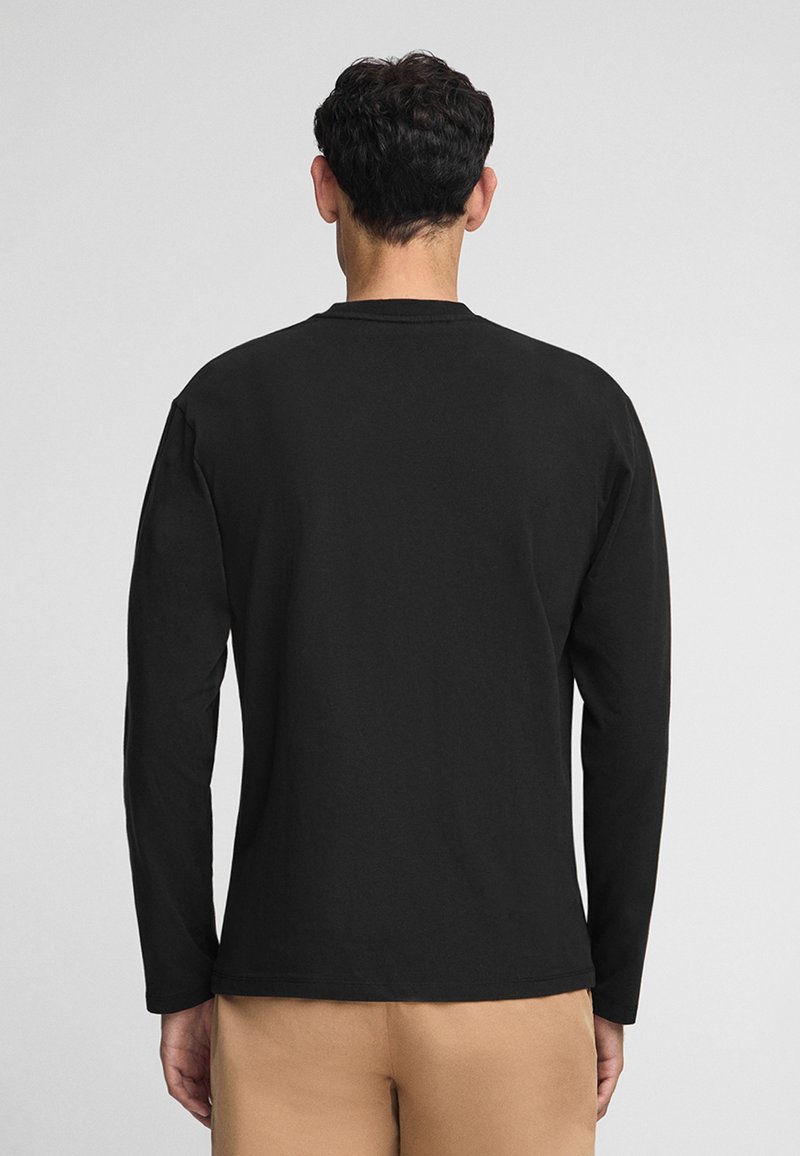 Czarna, długosługa koszulka z bawełny z okrągłym dekoltem i gładką fakturą, noszona z jasnymi spodniami.