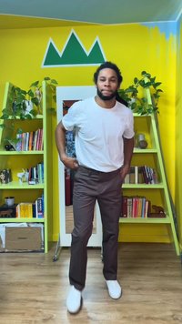 Hvit T-skjorte, brune bukser og hvite joggesko brukt av en person i et fargerikt rom med gule vegger og grønne detaljer.