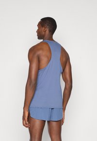 Débardeur de sport bleu avec un design dos nageur, fabriqué à partir d'un matériau texturé. Porté avec un short bleu assorti, affiché de l'arrière.