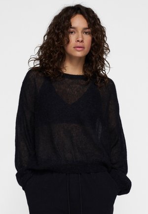 Maglione nero a maglia larga con maniche lunghe, scollatura rotonda e una trama trasparente, abbinato a pantaloni neri a vestibilità comoda.