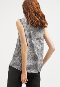 Černobílý tílko s paisley vzorem, volným střihem a kulatým výstřihem, vyrobené z lehké látky.