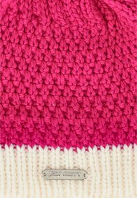 Stickad mössa med ett gradientmönster, med lysande rosa på toppen och en vit ribbad botten; inkluderar en metallmärkesetikett.
