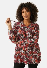 Kukallinen paita mustalla taustalla, jossa on punaisia, valkoisia ja vaaleanpunaisia kukkia. Pitkät hihat, joissa on joustavat hihansuut, ja V-pääntie.