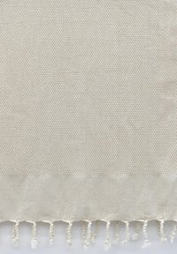 Beige strukturierter Stoff mit einem gewebten Muster, das an der unteren Kante mit gedrehten Fransen akzentuiert ist. Weiches, leichtes Material.